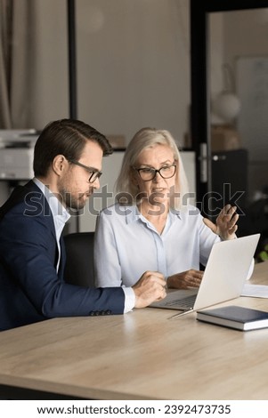 Confident younger and older business colleagues couple analyzing online project content, speaking at laptop, working together, talking on video conference call. Vertical shot Royalty-Free Stock Photo #2392473735