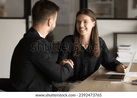 Couple of cheerful business partners shaking hands at workplace, smiling, discussing cooperation, partnership, ending negotiation, consultation meeting. Happy customer girl giving handshake to manager