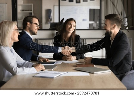 Positive satisfied business colleagues men starting cooperation with handshake, discussing successful project startup, shaking hands over negotiation table on team meeting Royalty-Free Stock Photo #2392473781