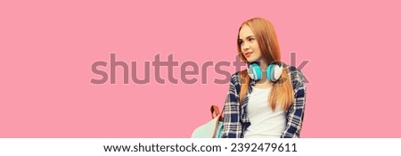 Portrait of happy smiling teenage girl in wireless headphones listening to music looking away on pink studio background, blank copy space for advertising text