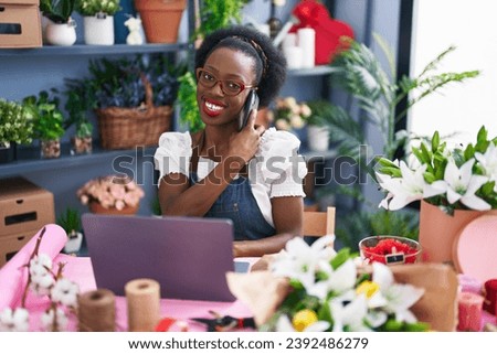 African american woman florist talking on smartphone using laptop at florist store