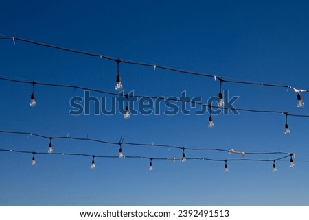 A garland of light bulbs in rows against a blue sky