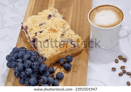 Indulge in the rich heritage of German tradition with a delectable sweet treat featuring a grape-filled pastry, sweet crumbly topping, a bunch of grapes, all set on a table adorned with a cup of coffe Royalty-Free Stock Photo #2392501947