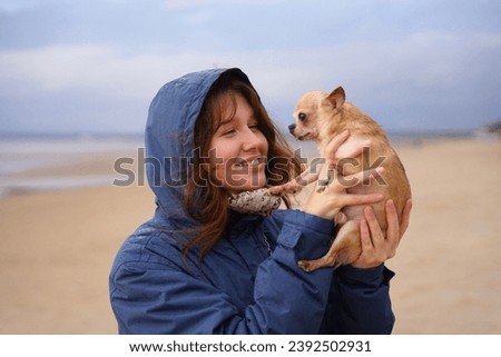 Happy young woman or teenager girl walking with her little pet Chihuahua or Toy terrier dog on the beach, hold puppy on hands. People love animals concept.