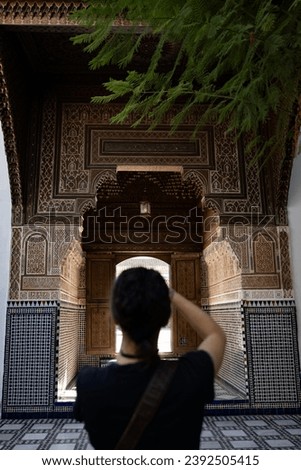 (Selective focus) Defocused girl in the foreground taking a photo at the Bahia Palace during a sunny day. The Bahia Palace in Marrakech is an impressive example of Moroccan architecture and design.