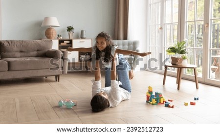Loving young Indian mother raise on outstretched arms her cute little 6s daughter, family play together, dreaming about travel feel untroubled and happy. Leisure, games with children at home concept Royalty-Free Stock Photo #2392512723