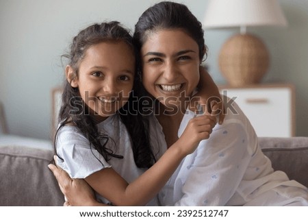 Loving mother and little child portrait, Happy Mother Day concept. Young Indian woman and preschooler daughter cuddling posing at home staring at camera feeling love spend leisure enjoy time together Royalty-Free Stock Photo #2392512747