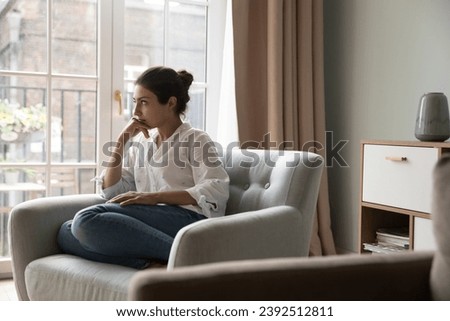 Worried young 25s Indian woman sit on armchair looks upset due to life concerns or break up, wait for boyfriend at home feels jealous, thinks over problems, search solution. Personal troubles concept Royalty-Free Stock Photo #2392512811