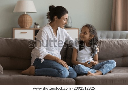 Indian mom and daughter talking sit on sofa. Mum having friendly warm conversation to little girl at home, share experience, give advice, teach child, express love, care. Family communication concept Royalty-Free Stock Photo #2392512825
