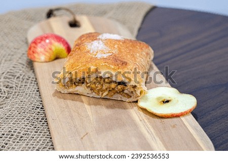 Delight in the authentic flavors of a traditional German apple strudel, elegantly presented on a wooden board, accompanied by a decorative ribbon of apple, on a beautifully set table