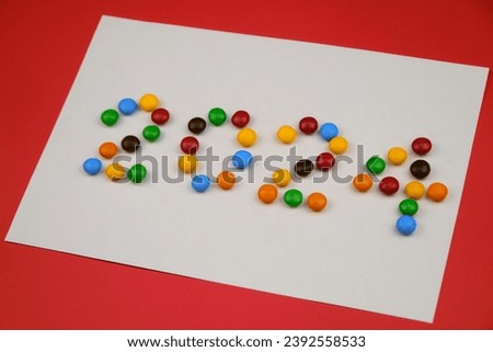 Happy New Year white paper red background, inscription 2024 laid out of round chocolate colored candies. Minimalistic Christmas greeting card