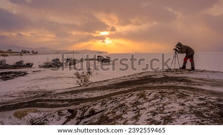 Photographer take pictures of the pier, Sunset and Winter landscape, abandoned fishery ships parked on snow at frozen lake Baikal, snow covered on ground, Russia.