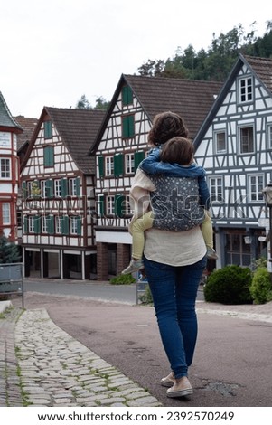Mother with her toddler in a baby carrier at her back while are having a walk in Schiltach in Black Forest, Germany. Drogerie is Apotheke Royalty-Free Stock Photo #2392570249