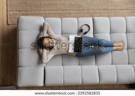 Above view woman rest on sofa with laptop and headphones, put hands behind head lying on couch fall asleep feels carefree looks calm enjoy weekend leisure, fresh conditioned air inside. Relax concept Royalty-Free Stock Photo #2392582835