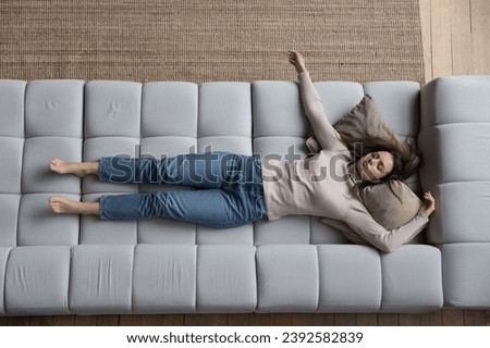 Young overworked woman looks drained, deprived of strength or vitality resting, sleeping alone at home lying on cozy sofa after hardworking, above view. Housewife and chores, exhaustion relief concept Royalty-Free Stock Photo #2392582839