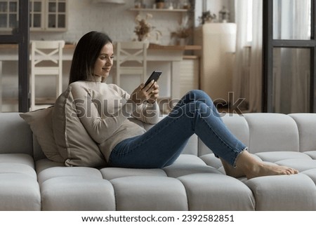 Pretty woman chat on-line via social media networks use cellphone resting seated on sofa at home, spend weekend on internet. Young gen and modern tech, remote communication, mobile apps usage concept Royalty-Free Stock Photo #2392582851