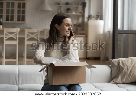 Happy woman, retail services client sit on sofa with courier parcel talks on cellphone, make call to contact support, thanks friend for gift, share positive feedback feel satisfied. E-commerce concept Royalty-Free Stock Photo #2392582859