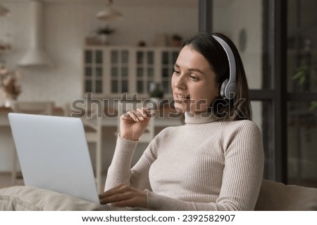 Young pretty woman in headphones sit on sofa with laptop take part in distance job interview at home use video call application. Remote communication to family, share news, vlogging activity concept Royalty-Free Stock Photo #2392582907