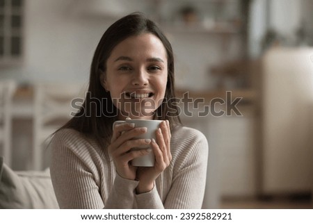 Portrait of beautiful young woman holding teacup sitting alone at home smile looks at camera. Peaceful female enjoy morning coffee beverage feel happy. New day with favourite drink, tea-time concept