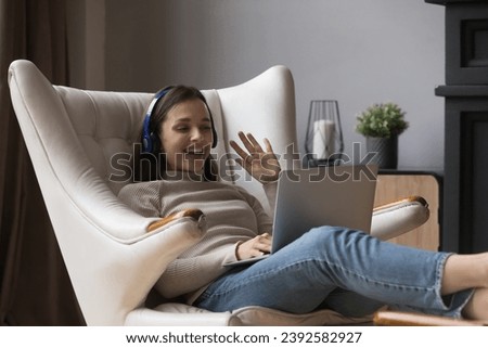 Happy beautiful young woman using laptop make video call relax seated on cozy armchair. Virtual meeting with family living abroad, video conference event use application, remote communication concept Royalty-Free Stock Photo #2392582927