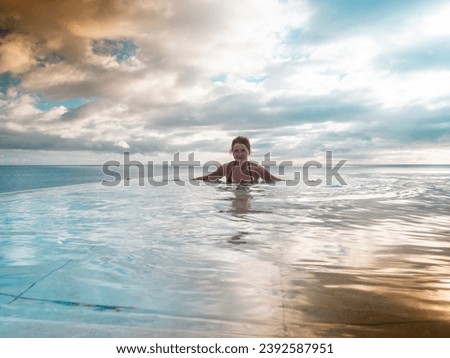 Mature caucasian woman is standing in an infinity pool and is looking over the sea