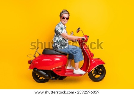 Full size photo of attractive senior woman riding red scooter wear trendy tropical print clothes isolated on yellow color background