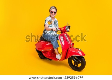 Full size photo of attractive senior woman riding red motorcycle wear trendy tropical print clothes isolated on yellow color background