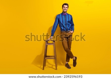 Full body photo of stylish man with bristle wear vintage bow tie standing near bar stool arm in pocket isolated on yellow color background