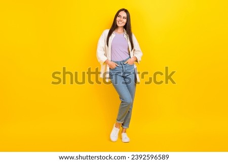 Full size photo of lovely girl wear white shirt denim trousers arms in pockets look empty promo space isolated on yellow color background