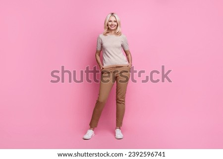 Full size photo of confident gorgeous person dressed striped t-shirt stylish pants hold hands in pockets isolated on pink color background