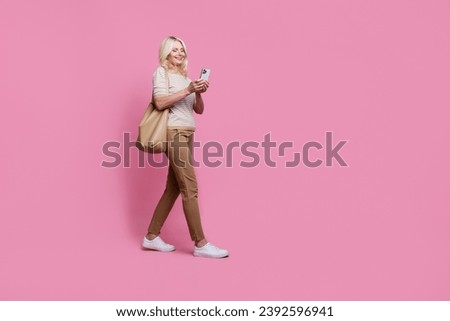 Full body profile photo of cheerful lady walk use smart phone texting empty space isolated on pink color background