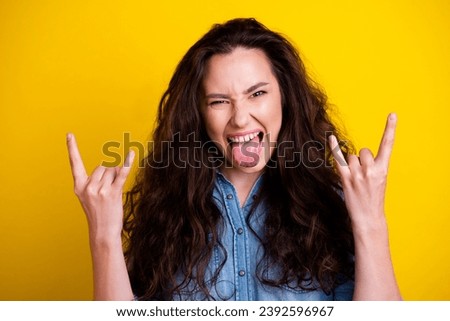 Portrait of overjoyed childish girl tongue out scream demonstrate heavy metal symbol isolated on yellow color background