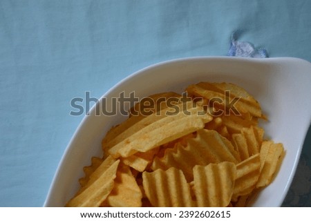 Portion of corrugated chips in a porcelain bowl served on the rustic wooden board. Traditional snack of Brazilian cuisine, fried potatoes