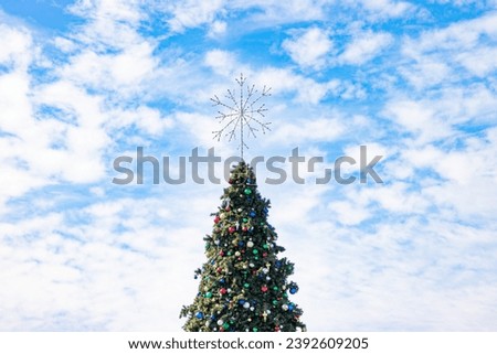 Christmas tree holiday with snowflake topper and ornaments against a partly cloudy December sky.