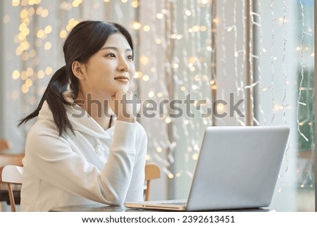 Young female college student model sitting at a table in an indoor cafe in South Korea, Asia, looking at a laptop, listening to a lecture, doing homework, or working	 Royalty-Free Stock Photo #2392613451