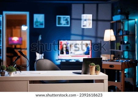 Empty home studio interior illuminated with neon lights at night, used for internet video production. Apartment filled with content creation equipment, TV running in blurry background Royalty-Free Stock Photo #2392618623