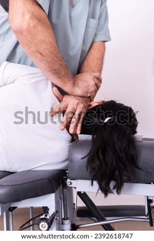 Vertical focused photo of a man hands massaging the neck of his female patient with his back to the camera. Cervicodorsal adjustment with drop