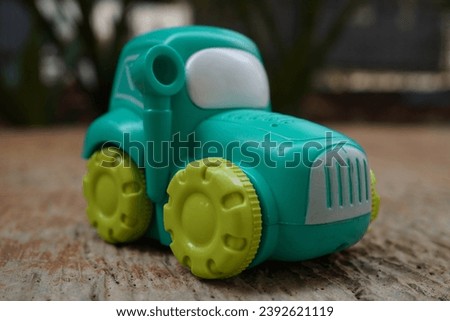 Close-up photo of a turquoise children's toy tractor with yellow tires. toy car child isolated