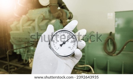 an engineer's hand is holding an analog thermometer used to measure the air temperature in the generator engine room, Checking the working temperature in the electric generator room.