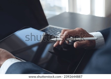 Business man hand with stylus pen using digital tablet with laptop computer on office table, closeup. businessman reading business e-document before signing electronic signature via mobile app