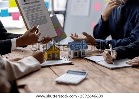 Real estate agents offer contracts to buy or rent housing. Businessman holding model small building house with property insurance at table in home sales office
