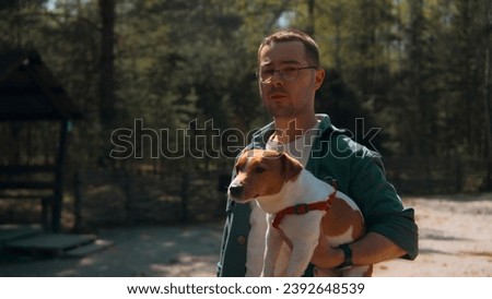 Man holds dog in arms in park. Stock footage. Handsome man with dog in arms walks in forest in summer. Man with dog on sunny summer day