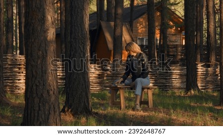 Young woman eating on bench alone in woods. Stock footage. Beautiful woman is sitting alone and eating in forest on sunny summer day. Young woman eats grill on bench in woods