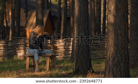 Young woman eating on bench alone in woods. Stock footage. Beautiful woman is sitting alone and eating in forest on sunny summer day. Young woman eats grill on bench in woods