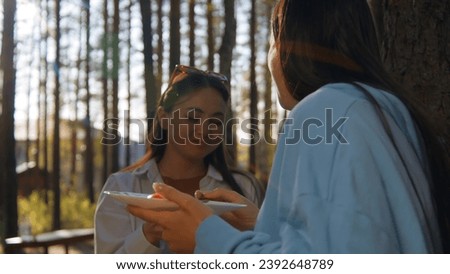 Beautiful young woman eating barbecue in nature. Stock footage. Two friends are standing and eating barbecue in forest on sunny summer day. Friends have fun eating in nature
