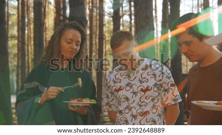 Friends communicate and eat food from barbecue in nature in summer. Stock footage. Friends are having fun talking and eating in woods on sunny summer day. Bright cheerful communication of friends in