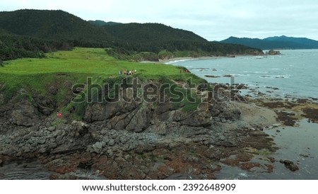 Top view of group of tourists on edge of sea cliff. Clip. Hikers on edge of rocky coastline. Tourists on edge of cliff of seashore on cloudy day Royalty-Free Stock Photo #2392648909