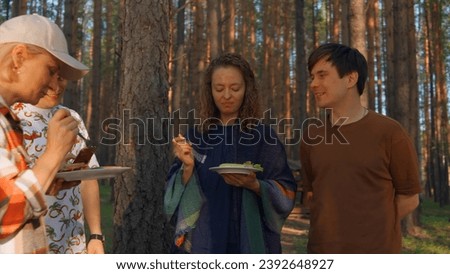 Friends eat barbecue from grill in woods. Stock footage. Friends relax in nature at barbecue and eat. Friends eat cooked meat on grill on sunny summer day