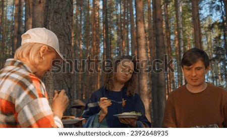 Friends eat barbecue from grill in woods. Stock footage. Friends relax in nature at barbecue and eat. Friends eat cooked meat on grill on sunny summer day