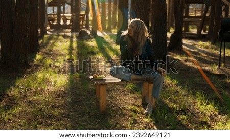 Pensive blond girl sitting alone on a small bench with a plate of vegetables. Stock footage. Woman in outdoors camp in the forest.
